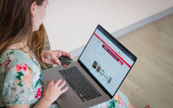 Woman in floral dress shopping online with a laptop and credit card indoors.