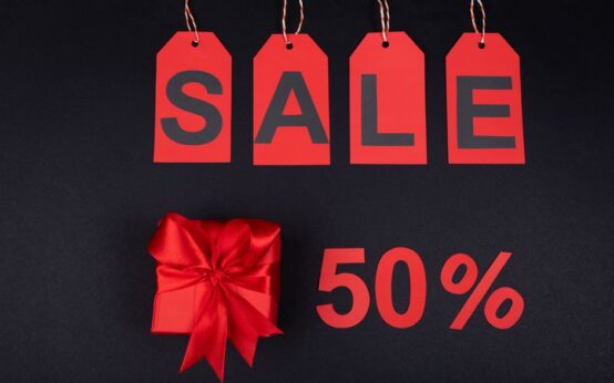 Red gift box next to sale tags and 50% sign on black background, ideal for promotions.
