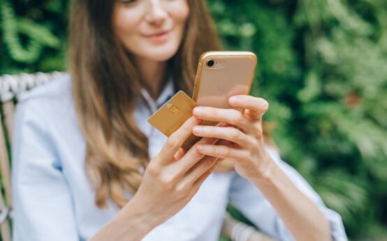 Woman using smartphone and credit card outdoors for online shopping.