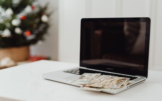 A laptop on a desk covered with cash, featuring a Christmas tree in the background.